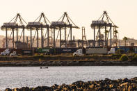 In this Tuesday, Oct. 19, 2021, photo trucks line up next to containers being shipped by rail in Terminal Island in Los Angeles. The Vincent Thomas Bridge suspension bridge, crossing the Los Angeles Harbor links San Pedro with Terminal Island. California Gov, Gavin Newsom on Wednesday, Oct. 20, issued an order that aims to ease bottlenecks at the ports of Los Angeles and Long Beach that have spilled over into neighborhoods where cargo trucks are clogging residential streets. Last week the White House allowed the ports complex to become a 24-hour operation in an effort to break the logjam and reduce shipping delays. (AP Photo/Damian Dovarganes)