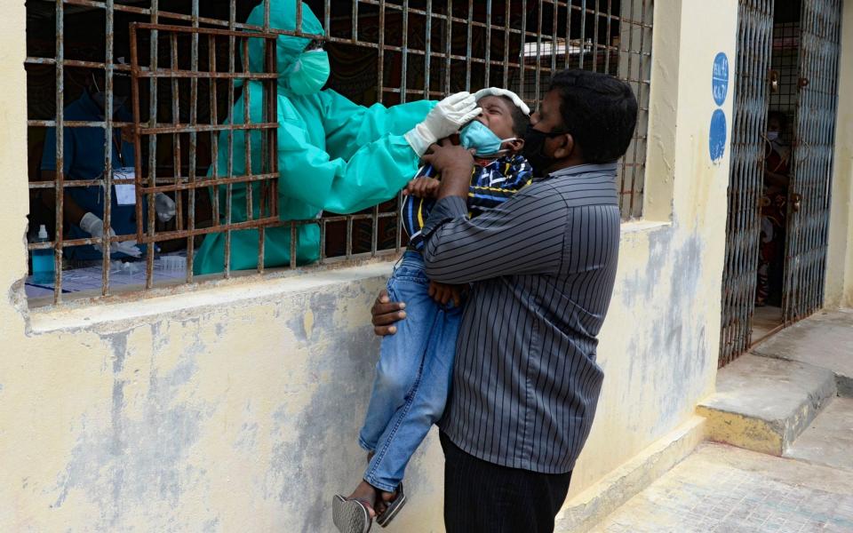 A man carries his son as a health worker collects a swab sample to test for the Covid-19 at a slum area in Hyderabad, India  - AFP