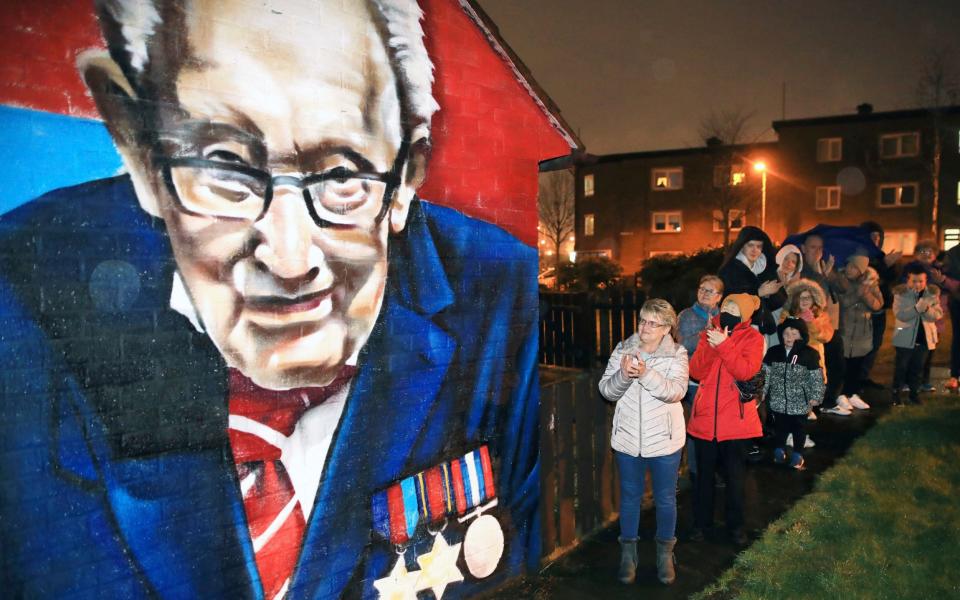 Local residents join a national clap beside a mural of Captain Sir Tom Moore in East Belfast, Northern Ireland, Wednesday - AP Photo/Peter Morrison