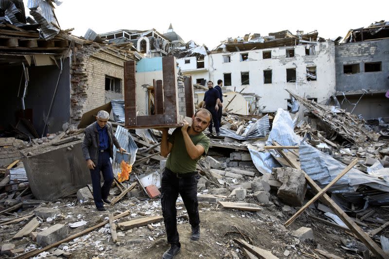 A man carries a table away from ruins at a blast site hit by a rocket during the fighting over the breakaway region of Nagorno-Karabakh in the city of Ganja