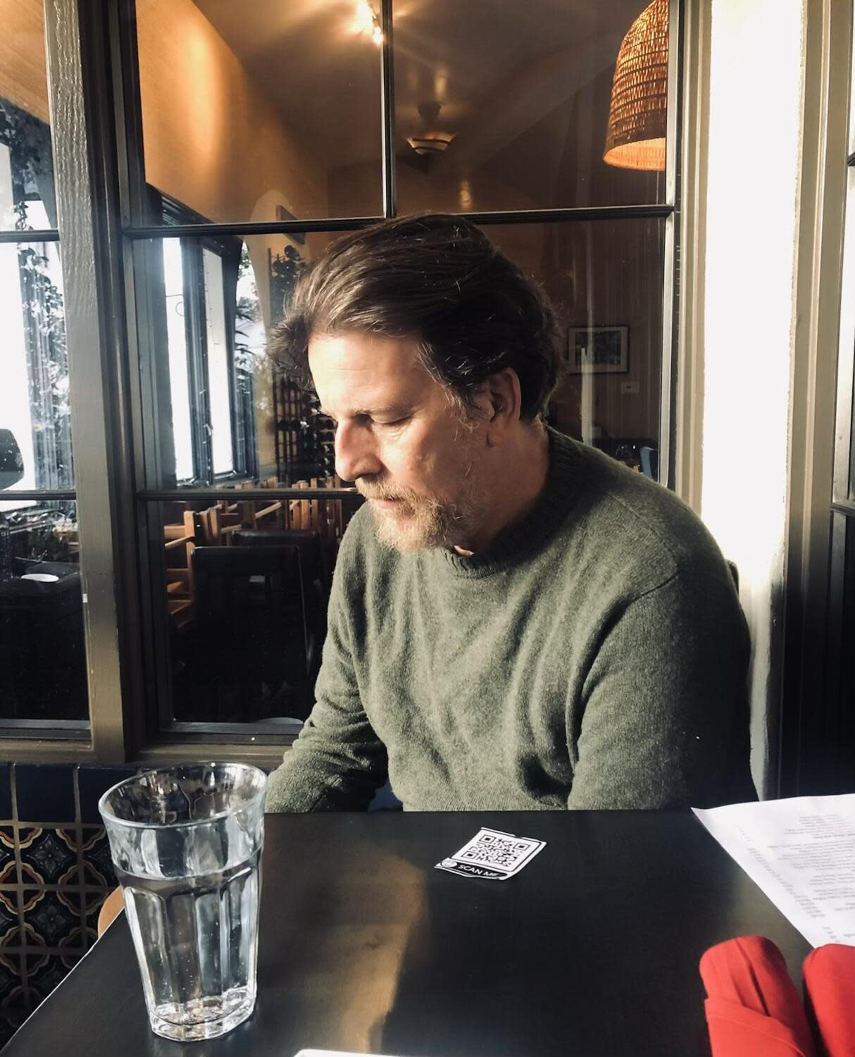 John Albert sits at a restaurant table, looking down