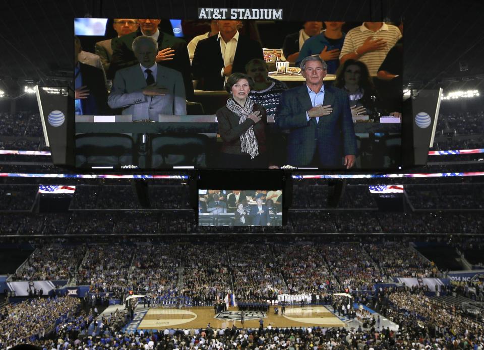 Former president George W. Bush and wife Laura are seen with former president Bill Clinton, left, on the overhead scoreboard during the national anthem before the NCAA Final Four tournament college basketball championship game between Connecticut and Kentucky, Monday, April 7, 2014, in Arlington, Texas. (AP Photo/Tony Gutierrez)