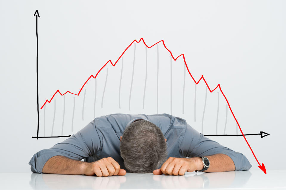 Man resting head on table in front of falling stock chart