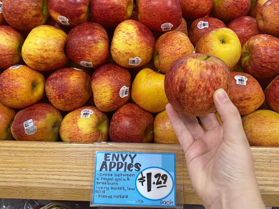 hand holding an envy apple in front of a stack of envy apples at trader joes