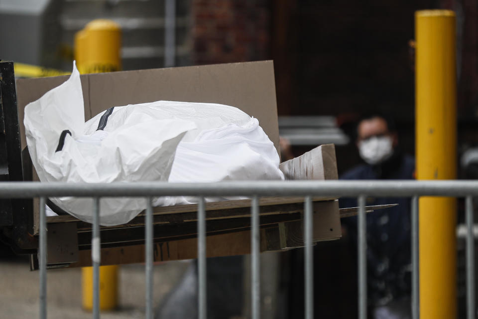 A body wrapped in plastic is loaded onto a refrigerated container truck used as a temporary morgue by medical workers due to COVID-19 concerns, Tuesday, March 31, 2020, at Brooklyn Hospital Center in the Brooklyn borough of New York. The new coronavirus causes mild or moderate symptoms for most people, but for some, especially older adults and people with existing health problems, it can cause more severe illness or death. (AP Photo/John Minchillo)