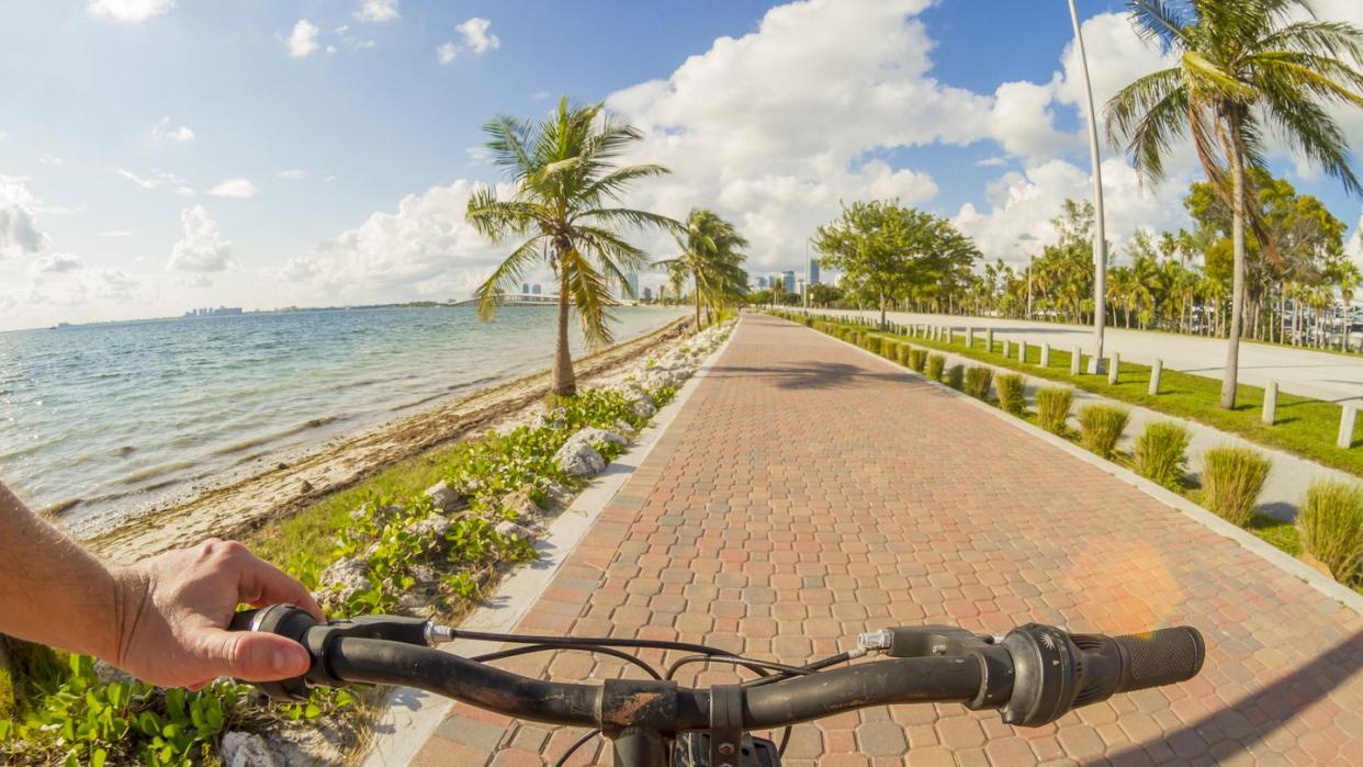 pov point of view shot of a young sport man riding a bicycle in front of a paradise blue sea landscape over a brick pathway bicycle line at key biscayne, miami beach, miami, south florida, united states of america usa
