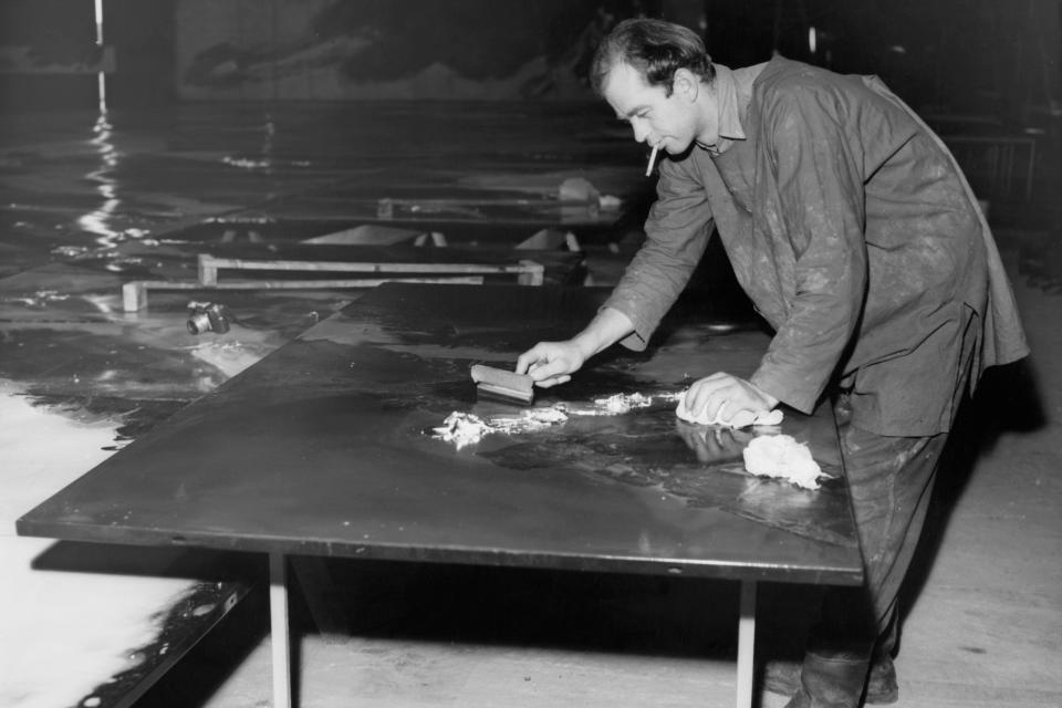 Black and white photo of Charles Lutyens leaning over a desk while smoking