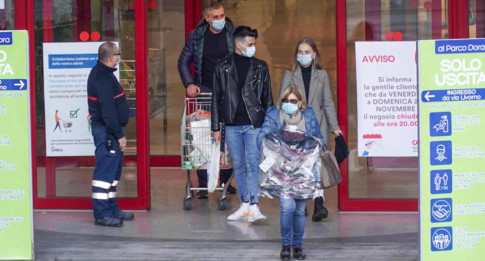 People walking out of a supermarket in Italy wearing face masks.