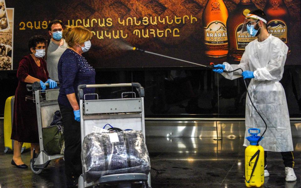 Passengers arriving in Armenia are sprayed down with disinfectant at the airport  - AFP / KAREN MINASYAN