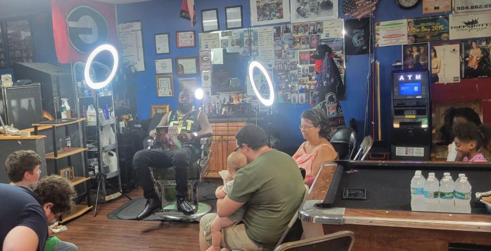 Cedrick Turner reads part of Hair Love, a young children's book, to kids whose families brought them to the Cutz-Linez & Trimz barbershop. The shop is the first location for the Unbanned Book Club