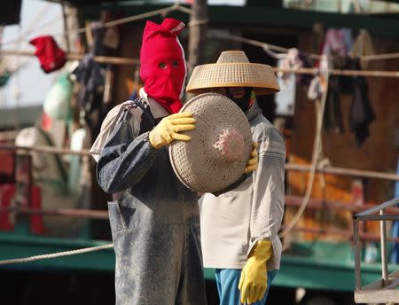 A man wearing a red face cover prepares to put on a hat as he repairs fishing nets at a port in the city of Dongfang on the western side of China's palm-fringed island province of Hainan, June 18, 2014. REUTERS/John Ruwitch