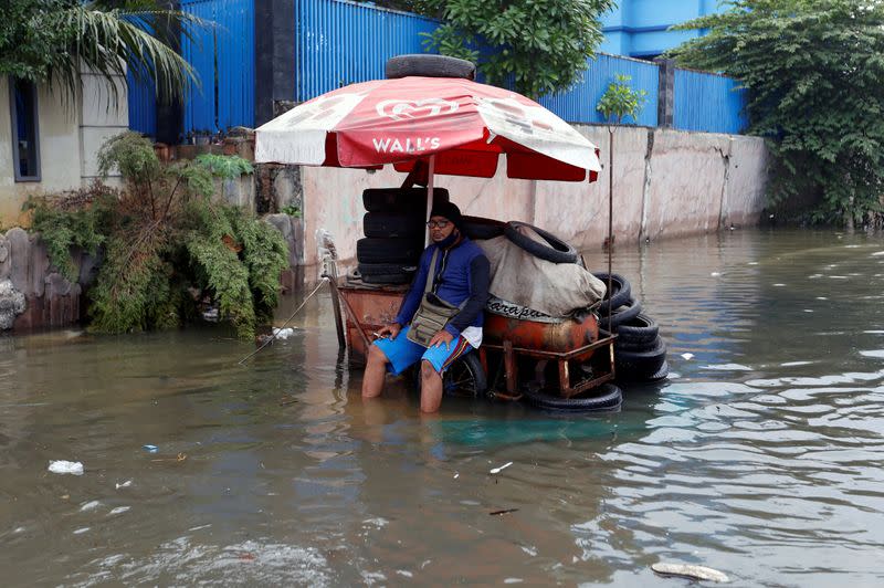A vendor sits on the cart at a flooded area affected by land subsidence and rising sea level in North Jakarta