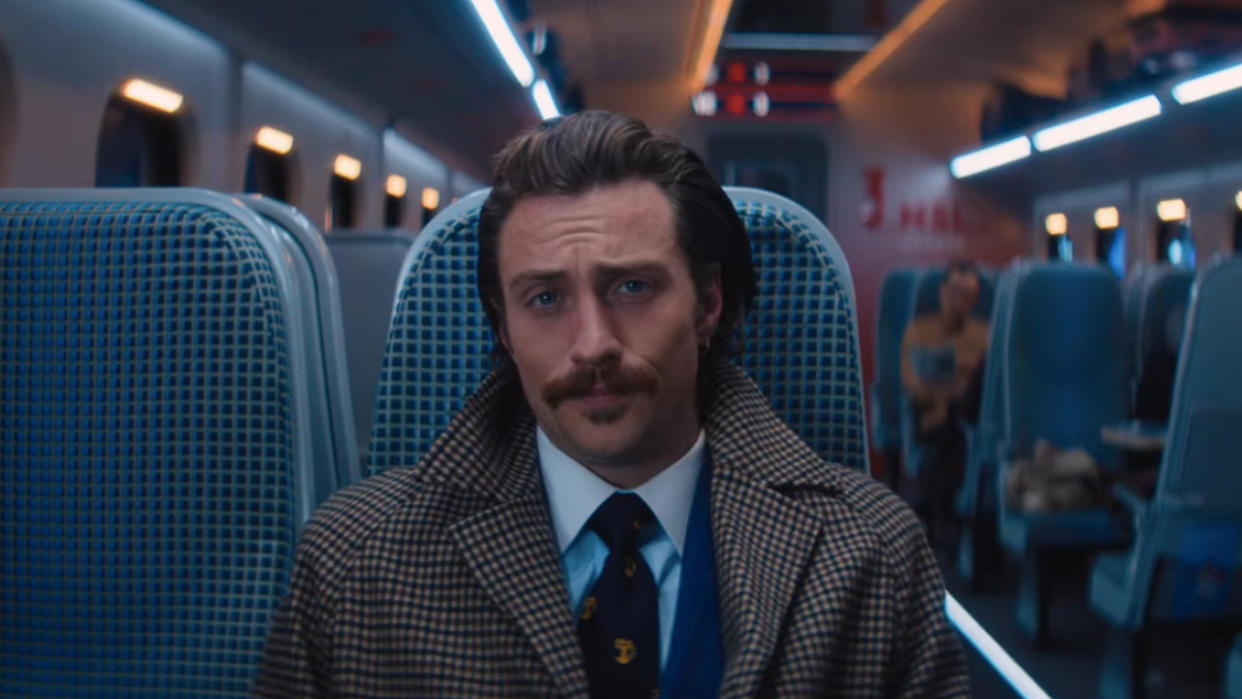  Aaron Taylor Johnson sitting in his seat, dressed sharply in Bullet Train. 
