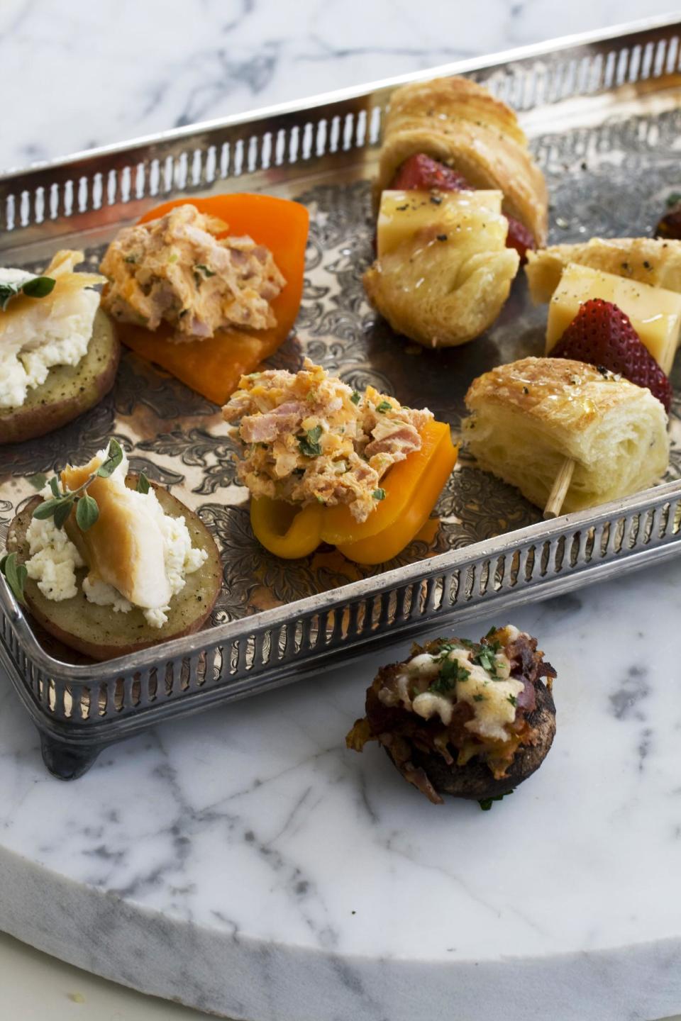 In this image taken on April 22, 2013, smoked schmeared potatoes, left, a chorizo hash stuffed mushroom cap, far right, stuffed baby bell peppers, second left, and strawberry croissant skewers are shown served on a tray in Concord, N.H. (AP Photo/Matthew Mead)