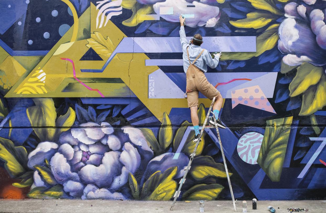 Streert Artist On A Ladder Painting Graffiti With Spray Paint