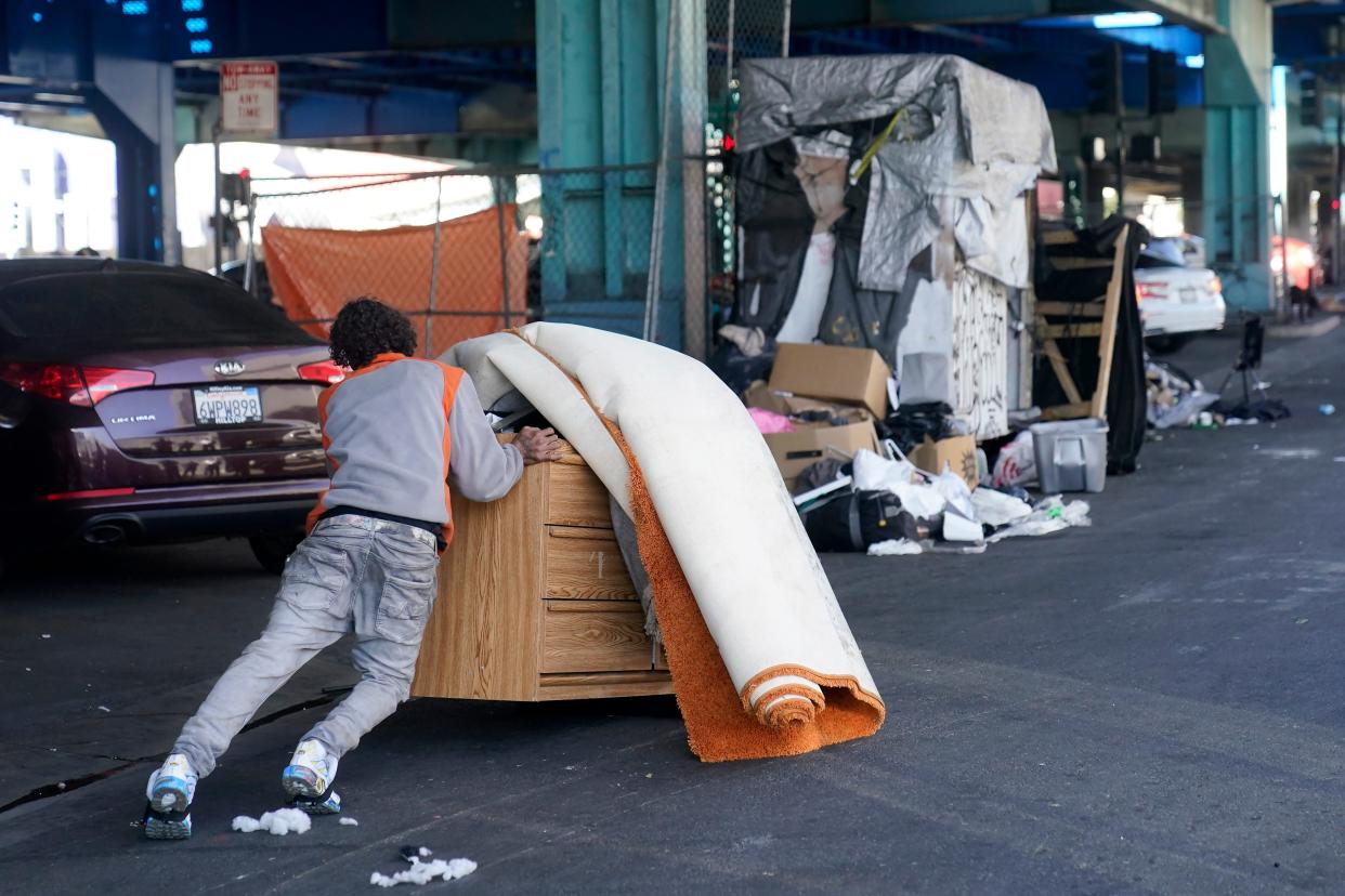 A man pushes items while a homeless encampment is being cleaned up in San Francisco, Tuesday, Aug. 29, 2023. Cities across the U.S. are struggling with and cracking down on tent encampments as the number of homeless people grows, largely due to a lack of affordable housing. Homeless people and their advocates say sweeps are cruel and costly, and there aren't enough homes or beds for everyone. (AP Photo/Jeff Chiu)