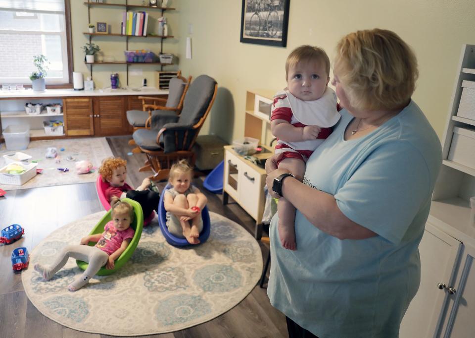 Nicole Leitermann of Impressions Family Child Care holds a baby as other children look on.