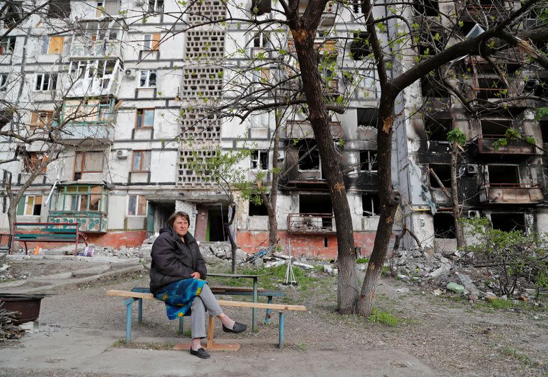 A local resident sits on a bench near a damaged apartment building in Mariupol