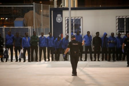 A police officer stands guard in front of migrants in the Center for Temporary Assistance to Foreigners (CATE) after disembarking from a rescue boat at the port of Malaga