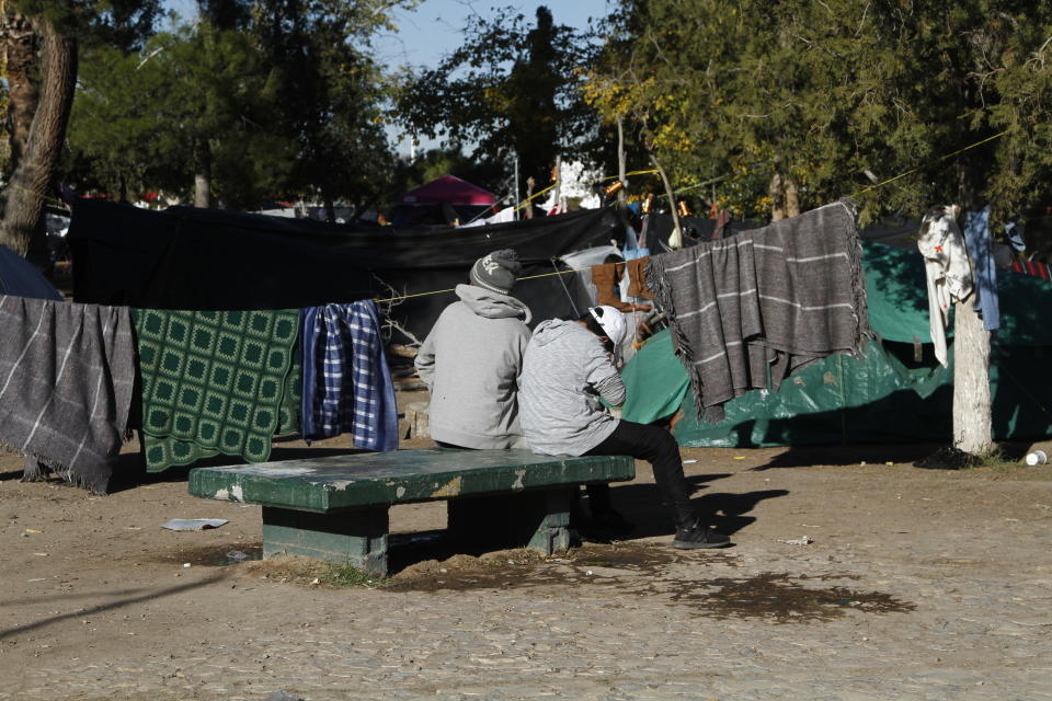 In this Tuesday, Dec. 3, 2019 photo, Luis, 38, left, a migrant fleeing gang violence in Michoacan, sits with his 13-year-old son on a bench in a public park facing a tent camp for refugees in Juarez, Mexico. Luis' family has lived in the camp for two months while they wait to apply for asylum in the U.S., at a border crossing about a quarter of a mile away. (AP Photo/Cedar Attanasio)