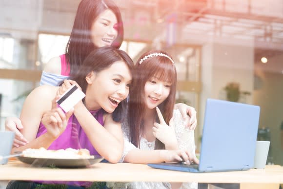 Three women looking at a laptop screen. One of them is holding a credit card.