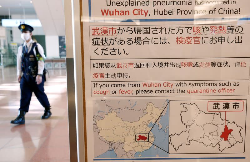 FILE PHOTO: A policeman wearing a mask walks past a quarantine notice about the outbreak of coronavirus in Wuhan, China at an arrival hall of Haneda airport in Tokyo