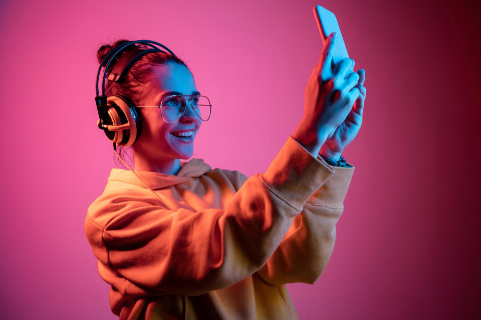 A young woman in glasses and headphones takes a selfie.