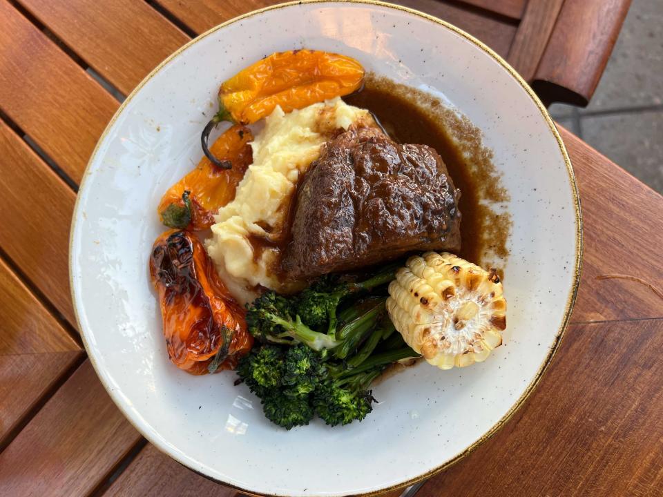 A dinner plate with short rib, mashed potato, corn, broccolini, and peppers.