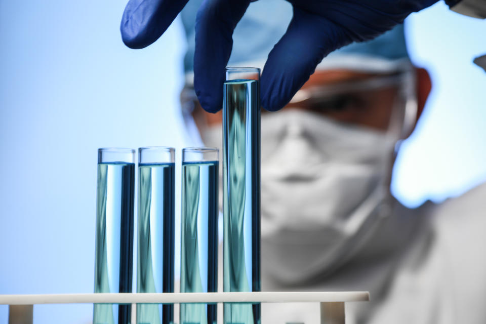 Scientist picking up a test tube with bluish liquid from a rack with three other test tubes.