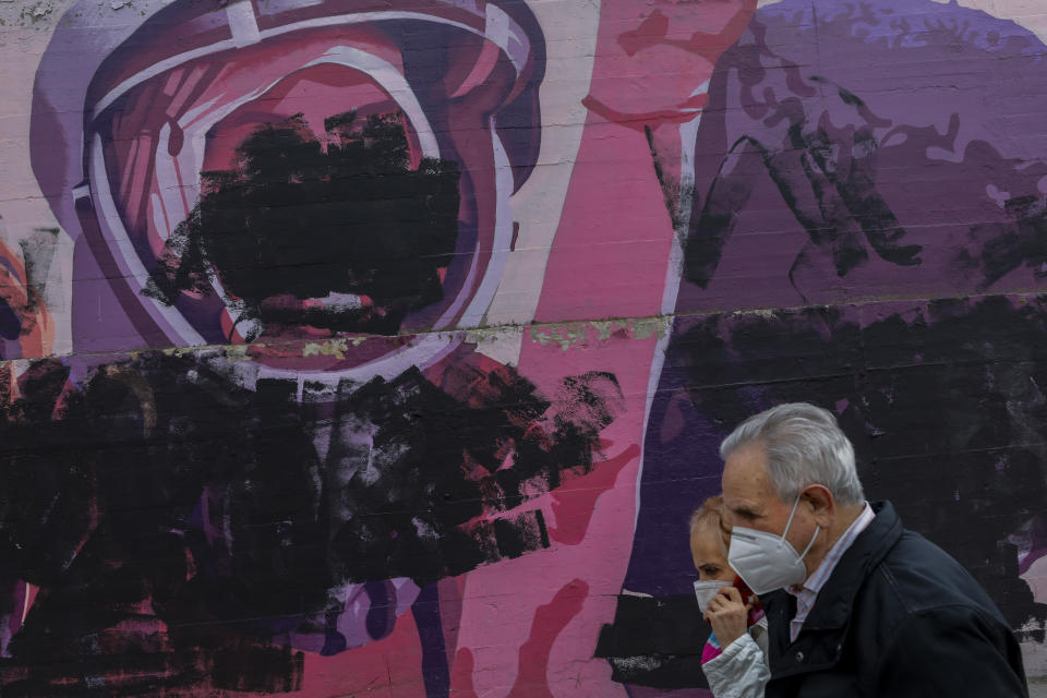 A couple walks past a vandalized mural depicting world's first woman cosmonaut Valentina Tereshkova in Madrid, Spain, Monday, March 8, 2021. At least two street murals celebrating accomplished women in politics, arts and science have appeared covered in black paint over the weekend. (AP Photo/Bernat Armangue)
