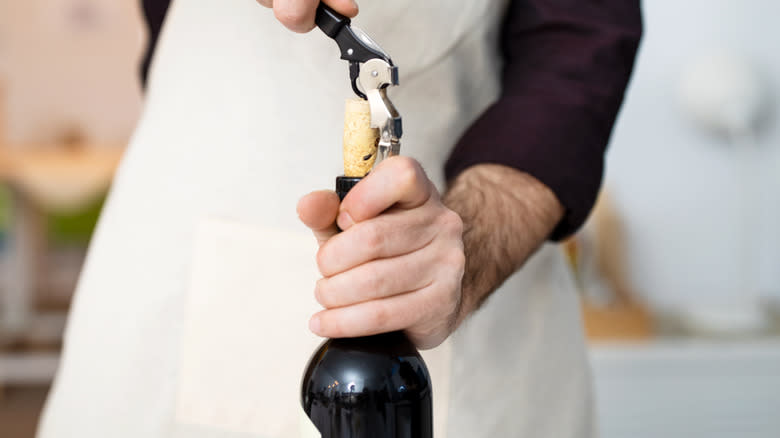 Person in apron uncorking wine
