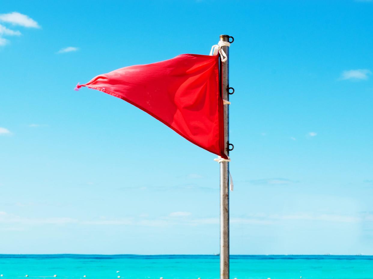 a triangle shaped red flag on a pole with a turquoise sky and sea background