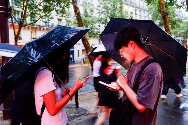 Dos personas observan la ceremonia en sus celulares, en París