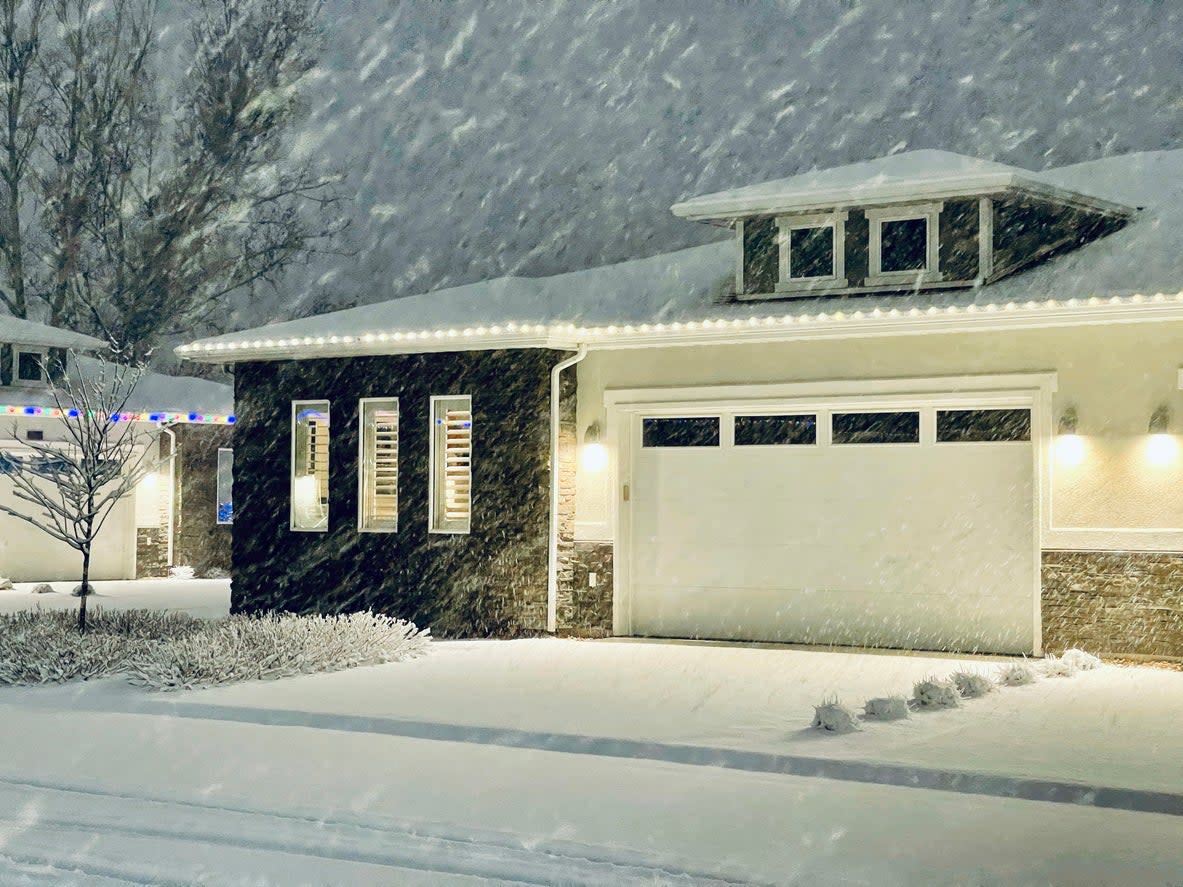 Midcentury style house in a snowstorm at dusk, with holiday lights on next door house.