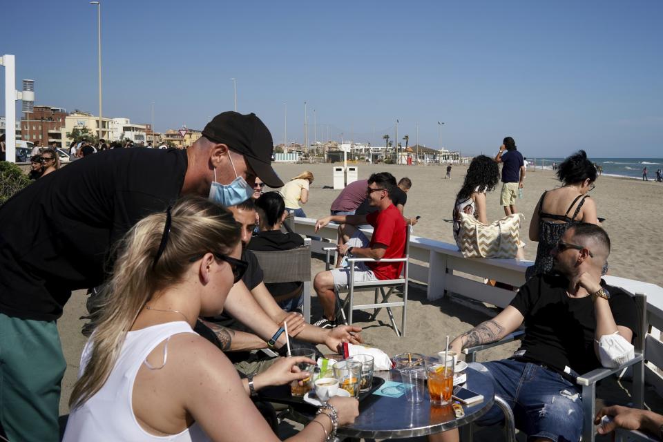 People sit at an outdoor cafè in Ostia beach, near Rome, Sunday, May 24, 2020. Europeans and Americans soaked up the sun where they could, taking advantage of the first holiday weekend since coronavirus restrictions were eased, while European governments grappled with how and when to safely let in foreign travelers to salvage the vital summer tourist season. Italy, which plans to open regional and international borders on June 3 in a bid to boost tourism, is only now allowing locals back to beaches in their own regions — with restrictions. (AP Photo/Andrew Medichini)