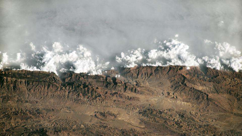  A satellite photo of a wall of haze and cloud trapped behind a mountain range. 