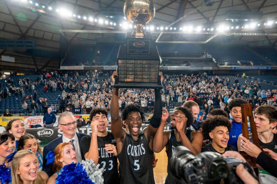 Zoom Diallo (5) hoists the state championship trophy as Curtis players celebrate beating Olympia, 49-43, to win the Class 4A title for the second consecutive year on Saturday, March 4, 2023, in Tacoma, Wash.