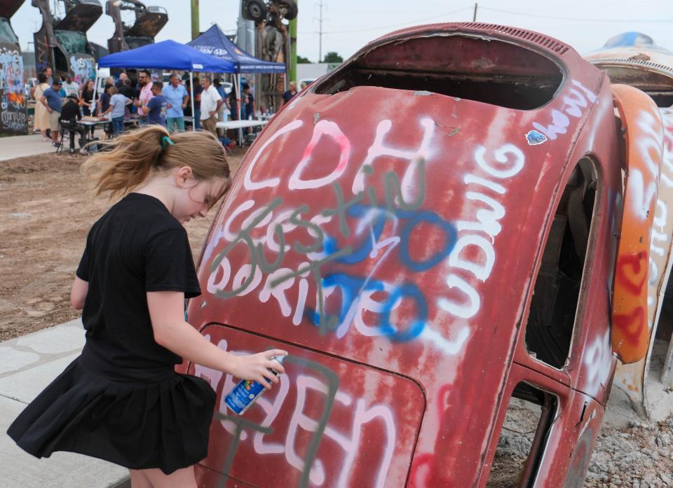 A young girl paints a newly planted Volkswagen Beetle Friday at the christening of the new Big Texan Route 66 Bug Ranch in Amarillo.