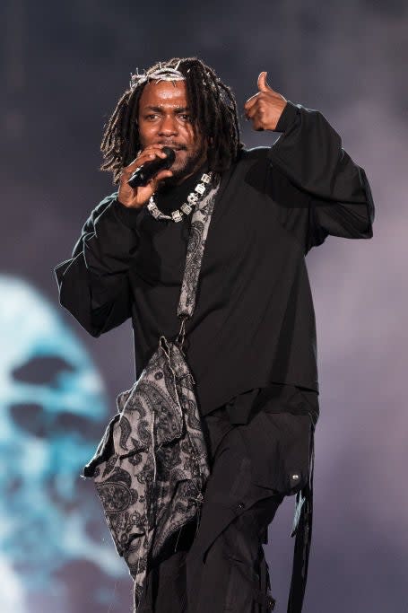 Kendrick Lamar performs on stage, wearing a loose black outfit and holding a microphone