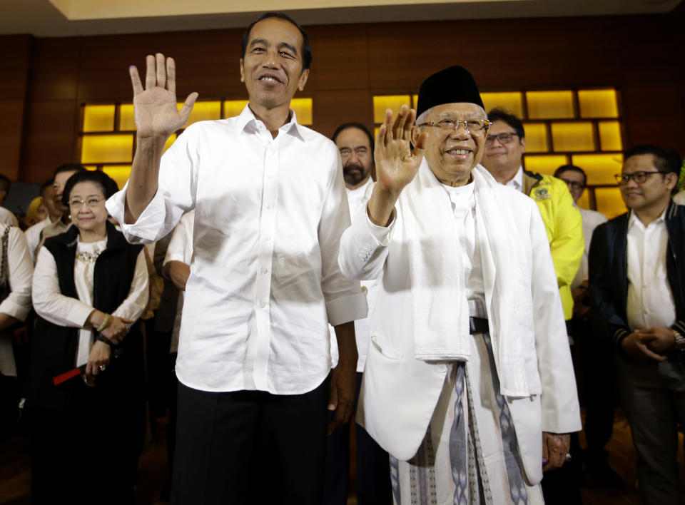 Indonesian President Joko Widodo, left, and his running mate Ma'ruf Amin wave to journalists after a press conference in Jakarta, Indonesia, Wednesday, April 17, 2019. Widodo is on track to win a second term, preliminary election results showed Wednesday, in apparent victory for moderation over the ultra-nationalistic rhetoric of his rival Prabowo Subianto. (AP Photo/Achmad Ibrahim)