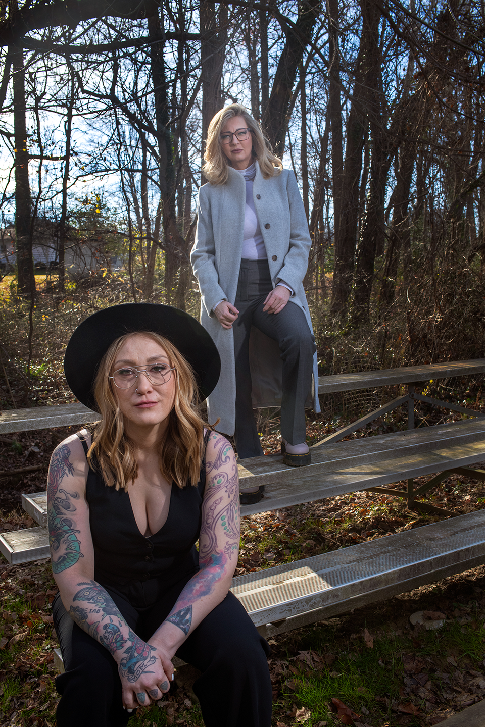 a woman sitting on a bench next to a woman standing on a bridge