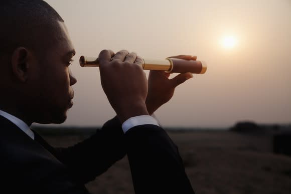 A man in a business suit looks through a telescope.