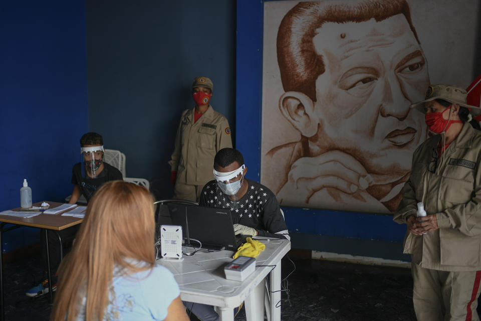 Members of the Venezuelan Electoral Council, sitting, wear face masks and shields amid the spread of the new coronavirus at a validation center, featuring a drawing of late President Hugo Chavez, to certify the authenticity of voter data in Caracas, Venezuela, Saturday, July 25, 2020. The legislative election is scheduled for Dec. 6 and thus far the opposition has indicated it will not participate. (AP Photo/Matias Delacroix)