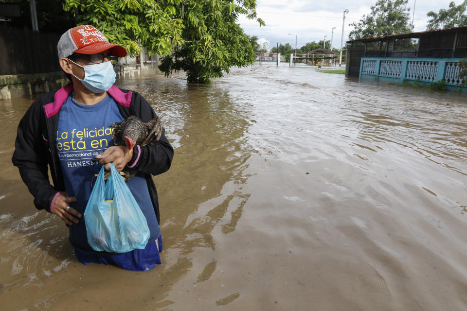 A resident, carrying a chicken, stands on a street inundated with floodwaters in the neighborhood of Planeta, Honduras, Thursday, Nov. 5, 2020. The storm that hit Nicaragua as a Category 4 hurricane on Tuesday had become more of a vast tropical rainstorm, but it was advancing so slowly and dumping so much rain that much of Central America remained on high alert. (AP Photo/Delmer Martinez)