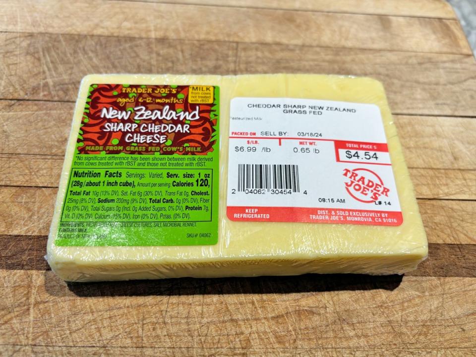 A rectangular block of white cheese with a brown and green label reading "New Zealand sharp cheddar cheese"