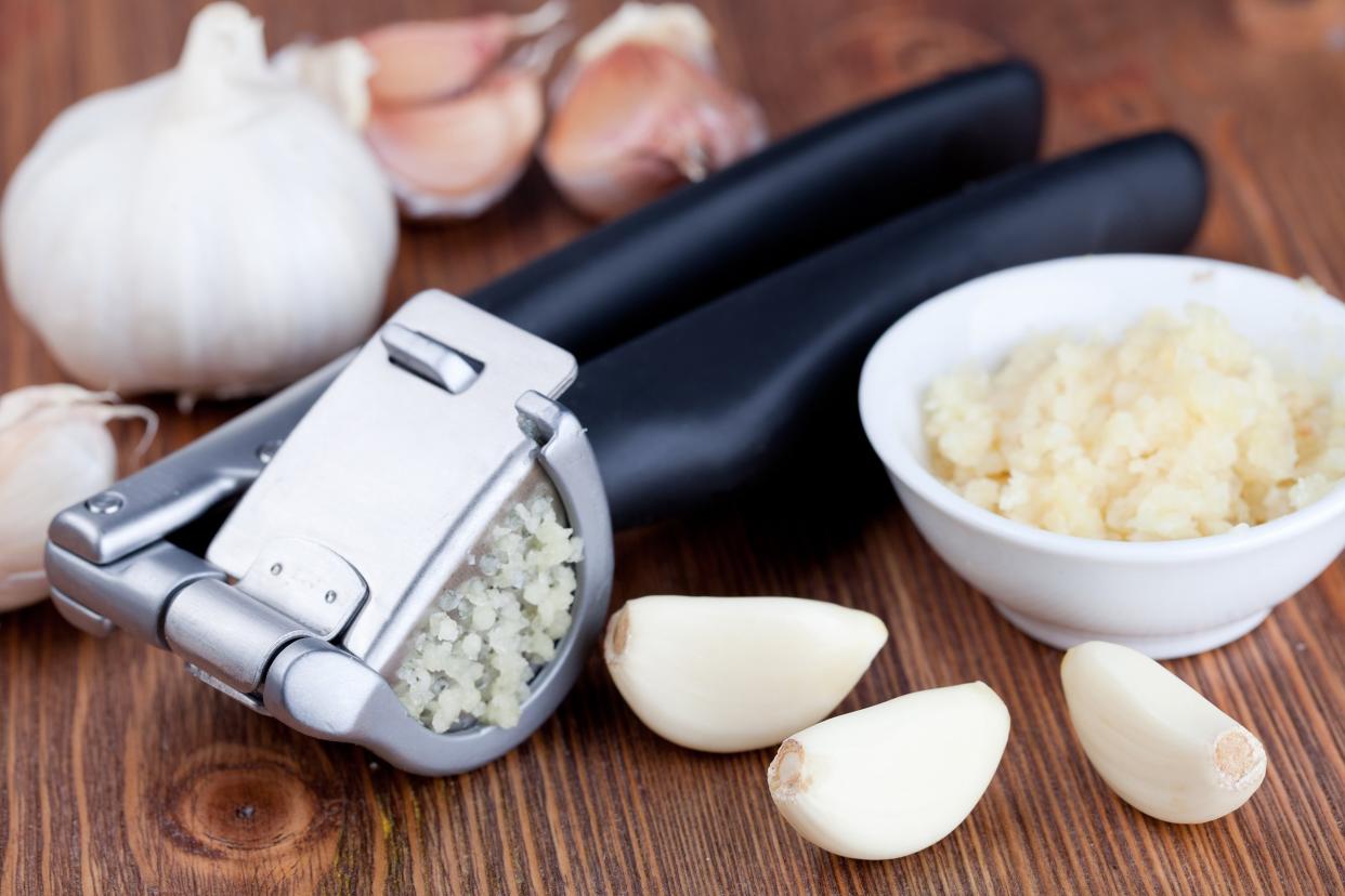 Garlic press on a cutting board with garlic