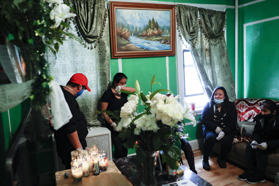 Sara Cruz, center, wife of the late Raul Luis Lopez who died from COVID-19 more than a month earlier, wipes tears from her eyes with her wrist after an in-home service for her husband performed by the Rev. Fabian Arias, Saturday, May 9, 2020, in the Corona neighborhood of the Queens borough of New York. (AP Photo/John Minchillo)