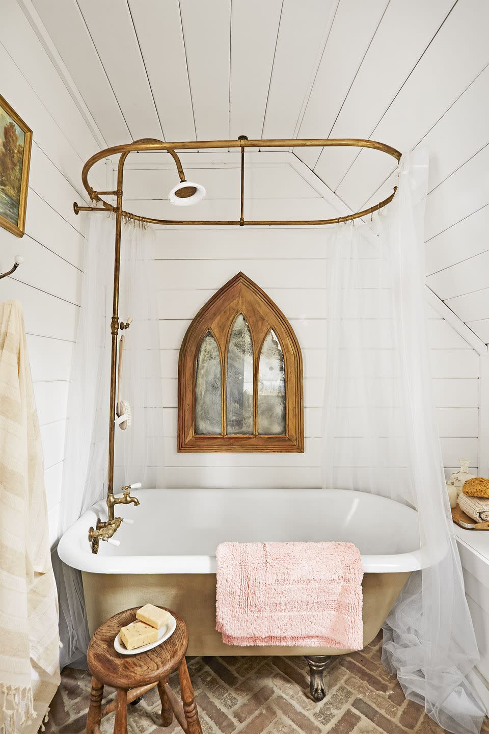 white wood paneled bathroom with sloped roof and cast iron tub with shower curtain, the floors are made from brick pavers laid in a herringbone pattern