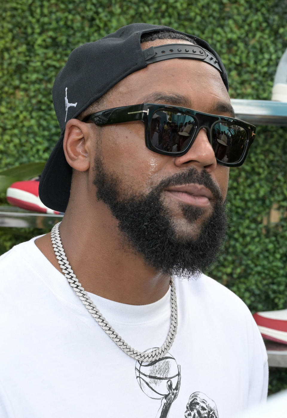 A close-up of Marcus walking outside. He's bearded and is wearing a basketball cap backwards and a chain