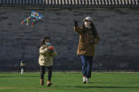 A woman and a child fly kite on a green outside a mall in Beijing, Sunday, Dec. 4, 2022. China on Sunday reported two additional deaths from COVID-19 as some cities move cautiously to ease anti-pandemic restrictions amid increasingly vocal public frustration over the measures. (AP Photo/Andy Wong)